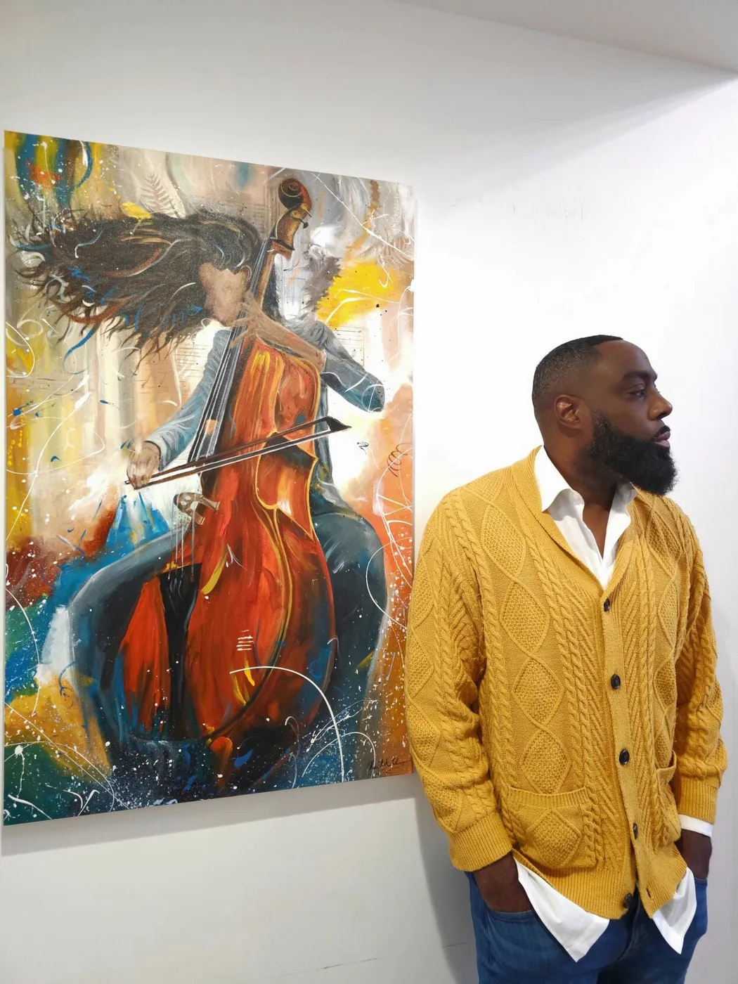 Neil Anthony Edwards in a mustard cardigan beside one of his paintings.